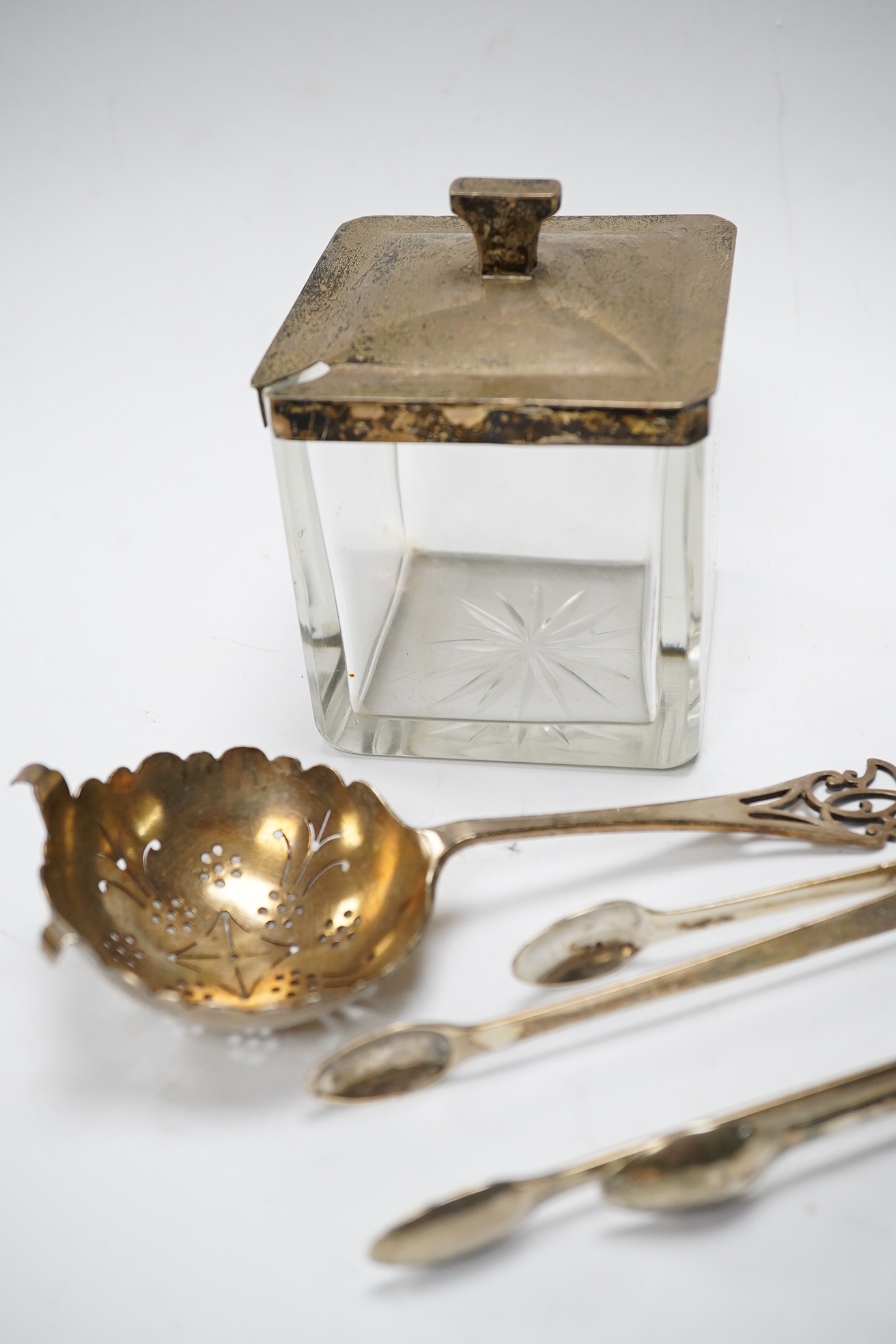 Two square silver topped glass preserve pot, two pairs of George III silver sugar tongs, a silver tea strainer and a caddy spoon. Condition - fair